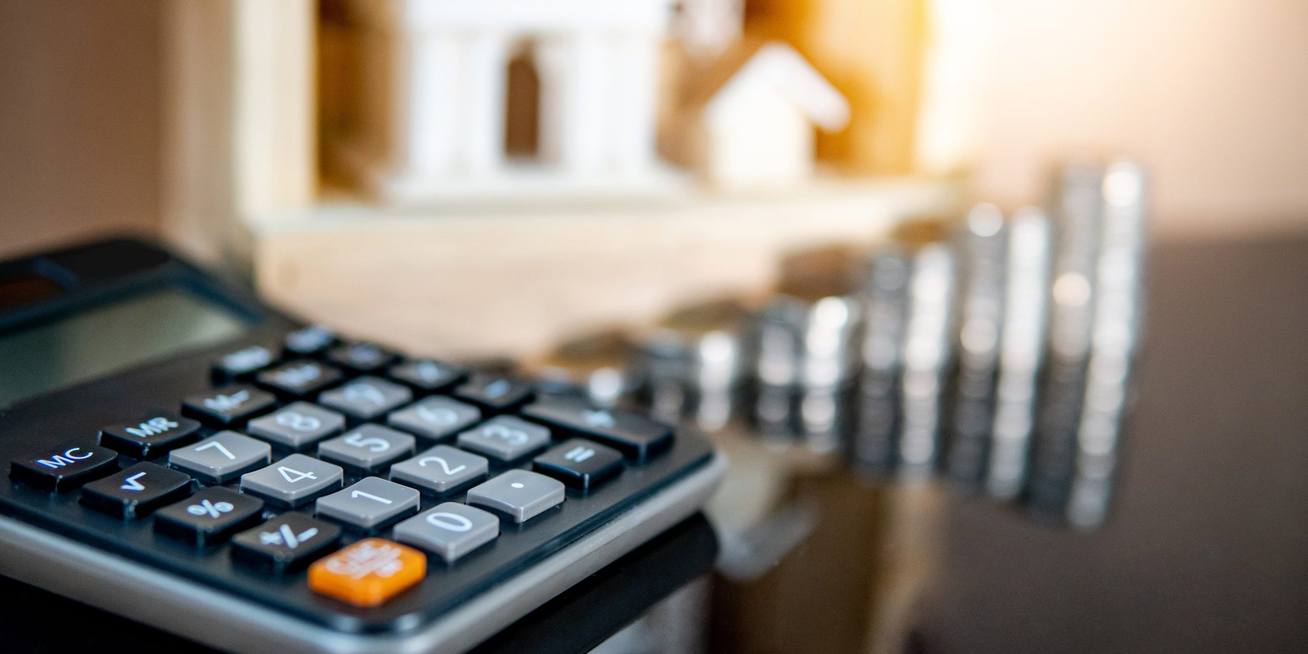Banking concept. Loan interest rate calculation. Saving money for property investment or real estate development. Home mortgage and lease. Coin stacked, house and bank models with calculator on table.